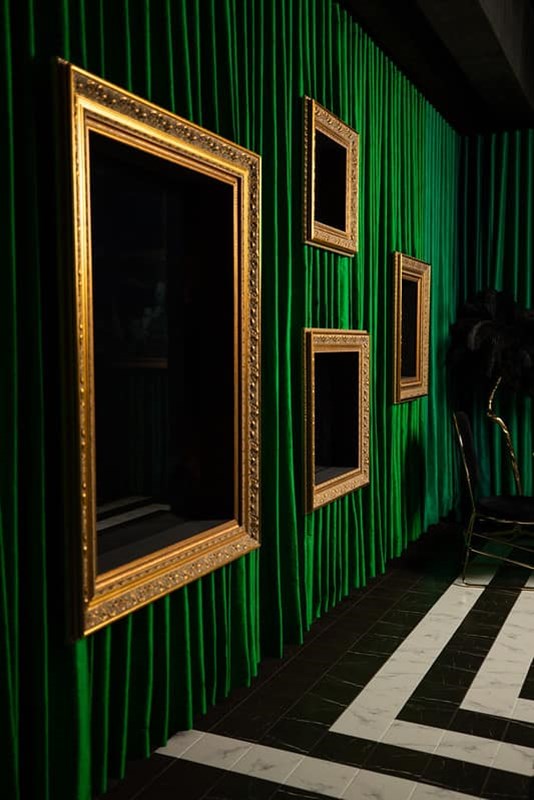 Frames with obscured artworks sit on top of a green curtain